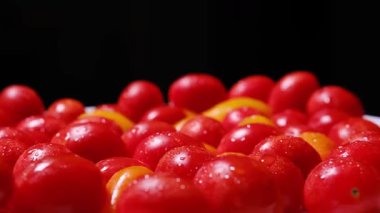 Kırmızı ve sarı kiraz domatesleri, koyu arkaplanda tatlı su damlacıklarıyla çok güzel parlar..