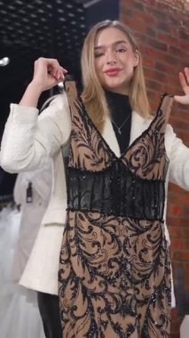 Zarif bir gelin butiği içinde zarif bir gece elbisesi seçen ince sarışın kadın. Dikey video. 