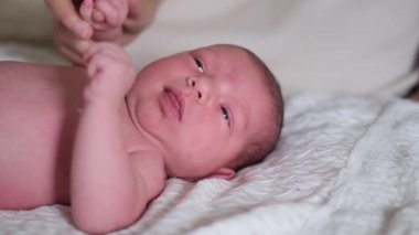 Yeni doğmuş harika bir bebek mutlu bir şekilde rahat, yumuşak bir battaniyeye uzanır ve nazikçe kameraya bakar..
