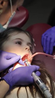 Pediatrik diş muayenehanesinde ağrısız bebek dişi tedavisi gören küçük bir kız. Dikey video. 
