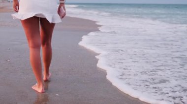 Bir kumsalda çıplak ayakla yürüyen bir kadın. Yumuşak okyanus dalgalarıyla. Yakın plan..