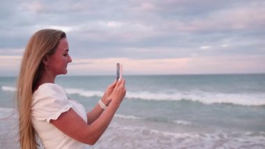 Telefonu denize çeviren gülümseyen kadın, o anın sakinliğinin ve güzelliğinin tadını çıkarıyor.. 