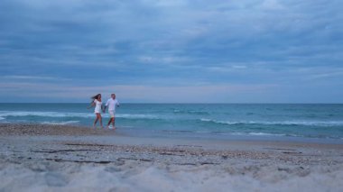 Çift kıyı boyunca neşeyle yürüyor, okyanus esintisinin ve birbirlerinin tadını çıkarıyorlar.. 