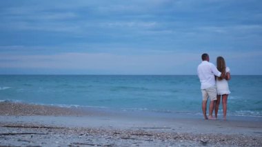 Birbirine aşık bir çift akşam ışığında okyanusun kenarında oturur ve kucaklaşır..