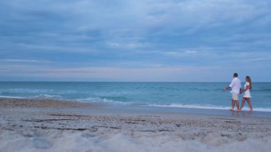 Sakin okyanus dalgaları ve bulutlu gökyüzü ile sisli bir kıyı şeridi boyunca yürüyen romantik bir çift.. 