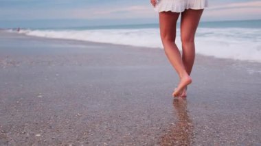 Gün batımında sahilde yalın ayak yürüyen huzur ve sükunetin tadını çıkaran bir kadın..