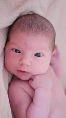 Yumuşak bir battaniyenin üzerinde huzur içinde yatan sevimli yeni doğmuş bebek, masumiyetini ve merakını gösteriyor. Dikey video.