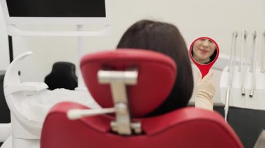 Bir hasta, klinikteki diş muayenesi sırasında aynada gülümsemelerini dikkatle inceliyor.