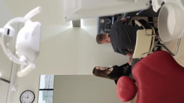 Profesyonel dişçi, diş muayenesi sırasında hastayla farklı tedavi seçeneklerini tartışıyor. Dikey video.