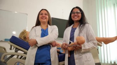 İki sağlık uzmanı, tıbbi eğitim sunan klinik bir ortamda eğitim bebekleriyle poz veriyorlar..