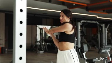 Genç bir kadın vücudunu esnetiyor ve modern bir spor salonunda egzersiz yapmaya hazırlanıyor..