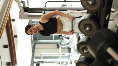 Odaklanmış bir kadın enerjik bir spor salonunda ağırlık kaldırıyor. Gücünü ve sağlığına olan bağlılığını gösteriyor.