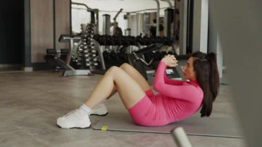 Genç bir kadın yoğun, modern bir spor salonunda vücut geliştirme eğitimine odaklanmış..