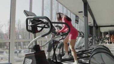 Çok kararlı bir kadın, parlak ve enerjik bir spor salonunda eliptik bir makinenin üzerinde güçlü bir şekilde egzersiz yapıyor..