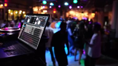 Canlı dinamik bir sahne, renkli ışıklar altında neşeli bir şekilde dans eden enerjik bir kalabalıkla bir DJ kurgusu sergiliyor.