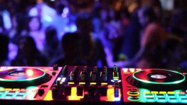 Canlı ve renkli bir DJ konsolu, canlı ışıklarla aydınlatılmış, dans eden büyük bir kalabalığın olduğu canlı bir partide..