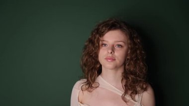 Canlı yeşil bir arka planda kıvırcık saçlı genç bir kadının güzel, sakin bir portresi..