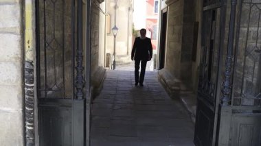 Yalnız siluetli bir figür, tarihi bir kemer yolunda zarifçe yürüyor, kentsel ortama bir entrika ekliyor..