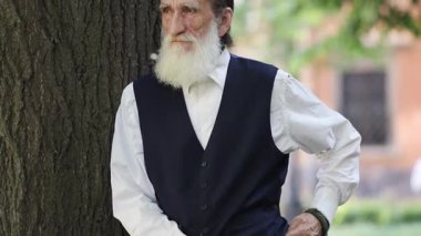 Seçkin bilge görünüşlü yaşlı adam huzur parkındaki sakin ağacın yanında düşünceli bir şekilde poz veriyor.. 