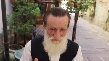 Uzun beyaz sakallı beyefendi büyüleyici bir sokakta rahatça oturuyor.. 