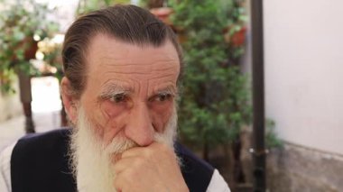 Derin düşüncelere dalmış yaşlı bir adam, sakin bir açık hava ortamında derin bir yansıma anı yakalıyor..