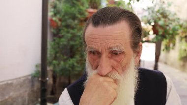 Doğayla çevrili güzel yeşil bir açık havada dikilirken düşünceli bir ifadeyle düşünceli bir şekilde bakan yaşlı bir adam..