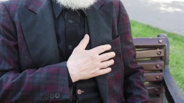 Resmi giyinmiş iyi giyimli bir adam bankta otururken kalp krizi geçiriyor..