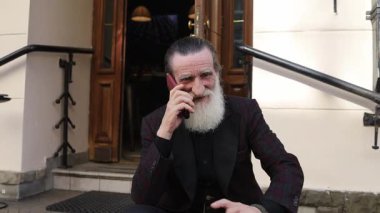 Sakalları budanmış bir beyefendi bir telefon görüşmesine dalmış, güzel günün tadını çıkarıyor.