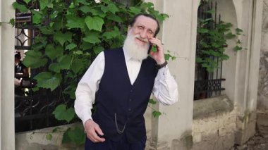 Geleneksel kültürel kıyafetli yaşlı adam yemyeşil ortamda dostça telefon konuşmasının tadını çıkarıyor.. 