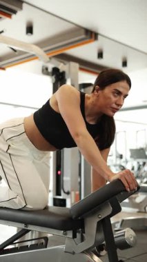 Kendini spora adamış bir kadın spor aletlerini kullanarak spor salonuna odaklanır.