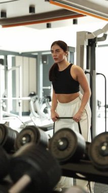 Odaklanmış bir kadın enerjik bir spor salonunda ağırlık kaldırıyor. Gücünü ve sağlığına olan bağlılığını gösteriyor.