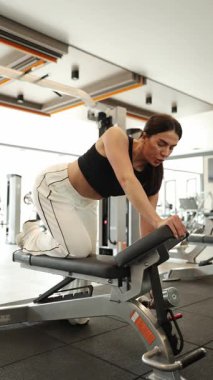 Fitness kızı her egzersiz sırasında formda ve teknikte kalmak için simülatörlerle antrenman yapar. Dikey video.