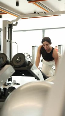 Spor salonunda ağırlık çalışan odaklı bir kadın modern bir spor salonunda çalışıyor. Dikey video