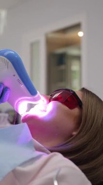 Etkili sonuçlar için LED ışığıyla diş beyazlatma prosedüründen geçen hasta. Dikey video. 