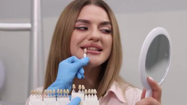 Bir kadın, potansiyel kozmetik geliştirme için çeşitli diş gözlüklerini denerken gülümsemesini dikkatlice inceliyor.