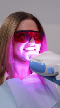 Profesyonel diş beyazlatma seansı göz kamaştırıcı gülümseme için gelişmiş LED ışık teknolojisi kullanıyor. Dikey video.