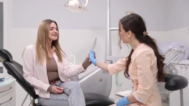 Bir dişçi, dişçi muayenesinde hastaya daha iyi anlamak için gülümsemelerini göstermek için ayna kullanır.