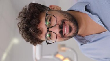 Kıvırcık saçlı ve gözlüklü neşeli bir adam enerji dolu bir ofiste diğerleriyle aktif olarak meşgul oluyor. dikey 