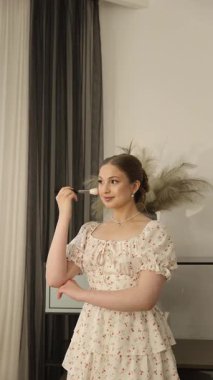 Çiçekli elbiseli genç bayan zarif bir şekilde makyaj yapıyor fırçayla, gösterişli güzellik ve zarafetle.. 