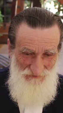 Uzun beyaz sakallı son sınıf öğrencisi, açık havada, pitoresk sokakta oturuyor. Dikey video. 