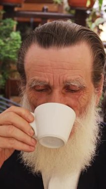 Yaşlı adam yeşil avluda kahvenin tadını çıkarıyor. Dikey video.