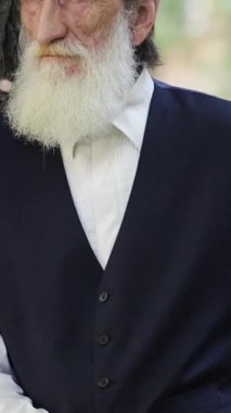 Seçkin ve düşünceli bir ifadeye sahip yaşlı adam sakin, yeşil bir parktaki sakin bir ağacın yanında duruyor. Huzur ve yansımayı çağrıştırıyor..