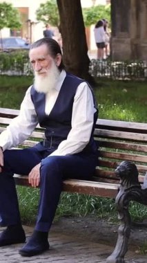 Huzurlu bir ortamda, güvercinlerle dolu bir bankta sakince oturan yaşlı adam. Dikey video. 