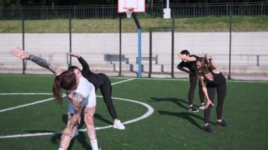 Farklı geçmişlerden canlı bir grup kadın bir açık hava futbol sahasında enerjik bir antrenmana katılarak, kapsayıcılığı, takım çalışmasını ve aktif yaşam tarzını ön plana çıkarıyor..