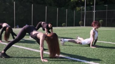 Spor meraklıları sıcak güneşin altında dışarıdaki canlı bir çimenlikte dinamik esneme hareketleri yapıyorlar..