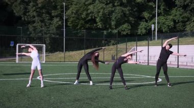 Spor yaparken, dışarıda futbol sahasında birlikte egzersiz yapan bir grup kadın..