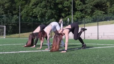 Üç sporcu güneşli bir futbol sahasında takım çalışması ve güç gösterisi yaparak antrenman yapıyorlar..