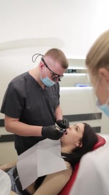 Bir dişçi, hastasını parlak, modern bir diş muayenehanesinde tedavi eder. Profesyonelliği, rahatlığı ve yüksek kaliteli sağlık hizmetlerini ön plana çıkarır. Dikey video.