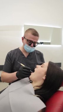 Modern bir klinikte dişçi muayenesi geçiren bir hasta, ileri derecede diş teçhizatı kullanan çok yetenekli ve deneyimli bir dişçi tarafından tedavi ediliyor. Dikey video.