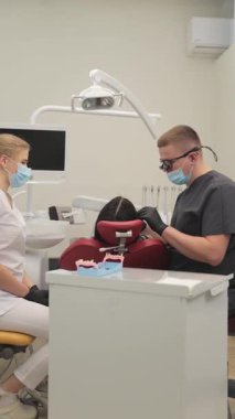 Erkek dişçi modern tıp kliniğinde diş tedavisi sırasında hastayı tedavi ediyor. Dikey video.